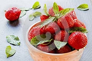 Fresh strawberries in white vintage bowl on black stone. Green mint leaves and ripe berries from garden on background