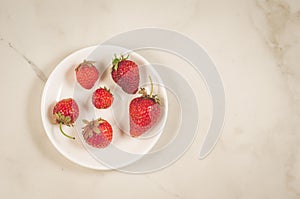 fresh strawberry berries in a white bowl/fresh strawberry berries in a white bowl on a marble background, top view and copy space