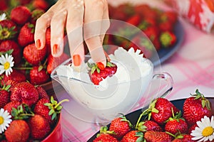 A fresh strawberry with cream in a bowl on a table in a summer garden is decorated with chamomile flowers the hand takes with a lo