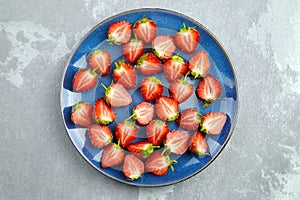 Fresh strawberry cut in half on blue ceramic plate on grey background