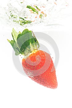 Fresh strawberry dropped into clear water with splash isolated on white background