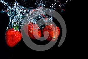 fresh strawberry dropped into water with splash on black backgrounds