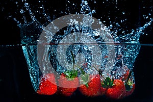 fresh strawberry dropped into water with splash on black backgrounds