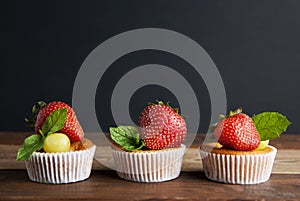 Fresh Strawberry fruits over homemade muffins on the plate decorated with mint leaves. Wooden table and black background. Copy spa