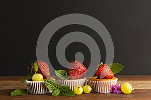 Fresh Strawberry fruits over homemade muffins on the plate decorated with mint leaves. Wooden table and black background. Copy spa