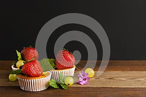 Fresh Strawberry fruits over homemade muffins on the plate decorated with mint leaves. Wooden table and black background. Copy spa