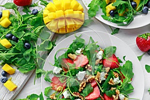 Fresh strawberry, mango, blueberrie salad with feta cheese, arugula on white plate