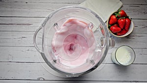 Fresh strawberry and milk into blender cooking milkshake, smoothie. Slow motion. Top view