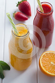 Fresh strawberry, orange smoothie in bottles with fruits on a white wooden rustic background