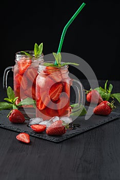 Fresh strawberry smoothie. Fresh summer cocktail with strawberries and ice cubes on a dark background on a black wooden table