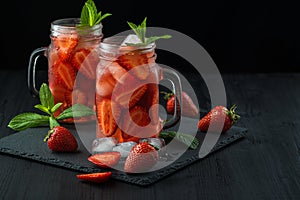 Fresh strawberry smoothie. Fresh summer cocktail with strawberries and ice cubes on a dark background on a black wooden table
