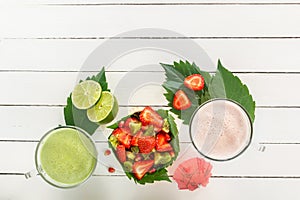 Fresh strawberry smoothies and vegetable green smoothies with lime and mint near a fruit salad of strawberries, kiwi