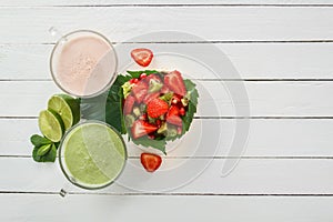 Fresh strawberry smoothies and vegetable green smoothies with lime and mint near a fruit salad of strawberries, kiwi