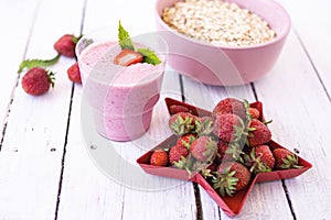 Fresh strawberry yogurt with berries around on a white wooden background. A pink shake in a glass, next to it is a pink cup with