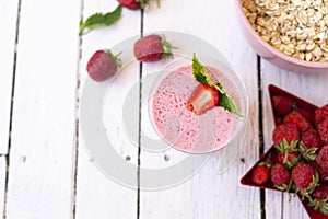 Fresh strawberry yogurt with berries around on a white wooden background. A pink shake in a glass, next to it is a pink cup with