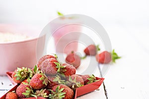 Fresh strawberry yogurt with berries around on a white wooden background. A pink shake in a glass, next to it is a pink cup with