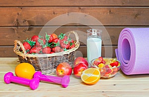 Fresh strawberry, yogurt, healthy fruit salad, fresh fruits, dumbbells and yoga mat on wooden surface