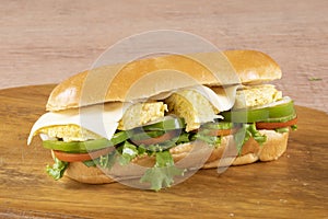 fresh submarine sandwiches with ham, cheese, bacon, tomatoes, lettuce, cucumbers and onions on dark wooden background