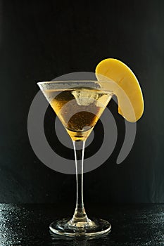 Fresh summer appletini cocktail in a martini glass with an apple slice on a black textured surface with water drops and reflection