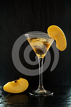 Fresh summer appletini cocktail in a martini glass with an apple slices on a black, wet textured surface with water drops and refl