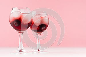 Fresh summer blueberry homemade lemonades in two goblets with ice cubes, berry in elegant pastel pink color kitchen interior.