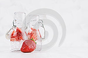Fresh summer cocktails with ripe strawberry, soda, bright bubbles in two yoke bottles on elegant soft light white wooden board.
