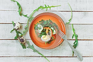 Fresh summer diet salad with arugula and quail eggs in an orange ceramic plate