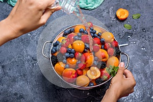 Fresh summer fruits and berries, apricots, blueberries, strawberries in colander, washing fruits and berries, woman`s hands