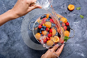 Fresh summer fruits and berries, apricots, blueberries, strawberries in colander, washing fruits and berries, woman`s hands, wate