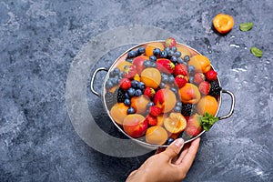 Fresh summer fruits and berries, apricots, blueberries, strawberries in colander,  woman`s hands holding bowl with fruits, summer