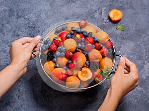 Fresh summer fruits and berries, apricots, blueberries, strawberries in colander, woman`s hands holding colander with fruits and