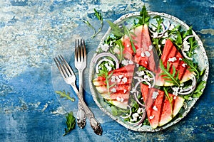 Fresh summer grilled watermelon salad with feta cheese, arugula, onions on blue background.