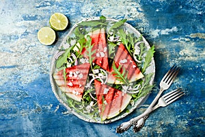 Fresh summer grilled watermelon salad with feta cheese, arugula, onions on blue background.