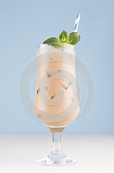 Fresh summer ice coffee in wet exquisite transparent glass with ice cubes, straw, green mint in light blue interior, vertical.