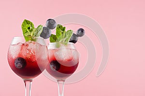 Fresh summer juicy cocktails in two goblets with ice cubes, blueberry, green mint in modern youth pastel soft pink color.