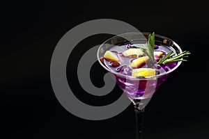 Fresh summer Purple rain cocktail in a martini glass with lemon slices on a black textured surface