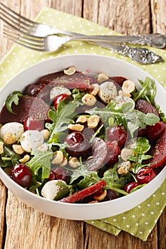 Fresh summer salad of arugula, baked beets, cherries, mozzarella, hazelnuts close-up in a bowl. Vertical
