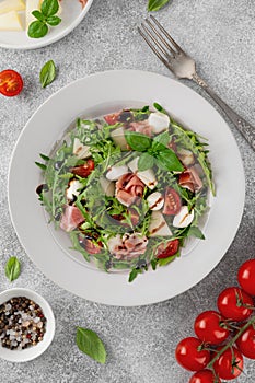 Fresh summer salad with arugula, melon, prosciutto and mozzarella cheese on concrete background, Healthy food. Top view