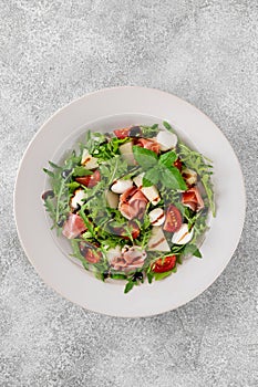 Fresh summer salad with arugula, melon, prosciutto and mozzarella cheese on concrete background, Healthy food. Top view