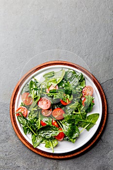 Fresh summer salad with baby spinach and tomatoes cherry. Top view, copy space. Slate gray background