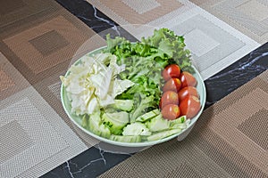 Fresh summer salad with early cabbage, cucumbers, tomato and lettuce in green plate on brown placemat. Green vegetable salad in