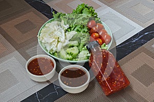 Fresh summer salad with early cabbage, cucumbers, tomato and lettuce in green plate with spicy sauce on brown placemat. Green