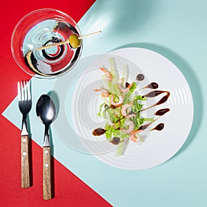 Fresh summer salad of shrimps, greens, celery, teriyaki sauce with cutlery, with martini glass on red and minty color with shadow.