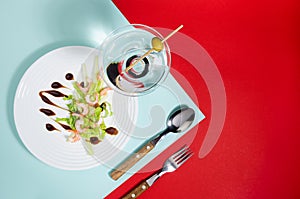 Fresh summer salad of shrimps, greens, celery, teriyaki sauce with cutlery, with martini glass on red and minty color with shadow.