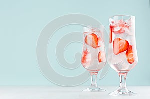 Fresh summer strawberry drink with red fruit pieces, ice cubes, tonic in two glasses light soft pastel  blue color background.