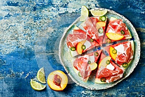 Fresh summer watermelon pizza with feta cheese, peach, prosciutto, jalapeno and honey drizzle on blue background.