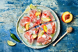 Fresh summer watermelon pizza with feta cheese, peach, prosciutto, jalapeno and honey drizzle on blue background.