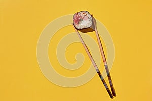 Fresh sushi roll and chopsticks on yellow background