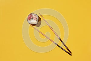 Fresh sushi roll and chopsticks on yellow background