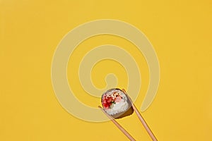 Fresh sushi roll and chopsticks on yellow background